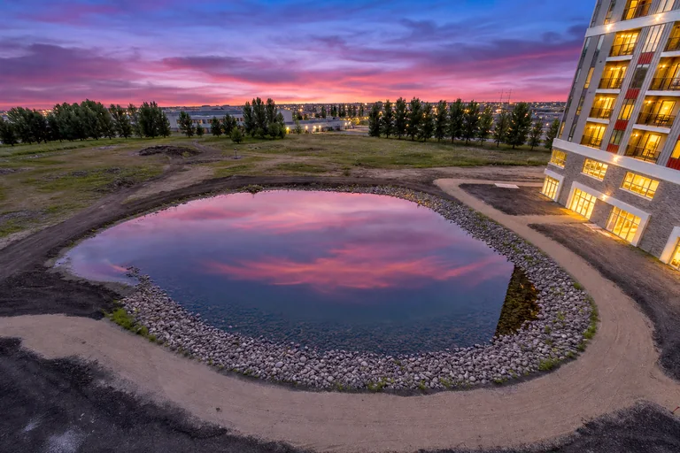 MAKT pond and walking path at sunset with illuminated apartment windows