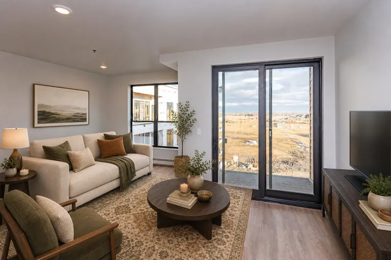 MAKT one-bedroom living area with kitchen view, wood-look flooring, and balcony door